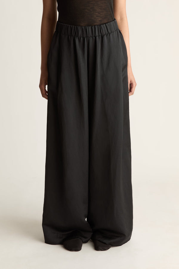 Close-up of black wide-leg pants with elastic waist and loose full leg, worn with a sheer black top