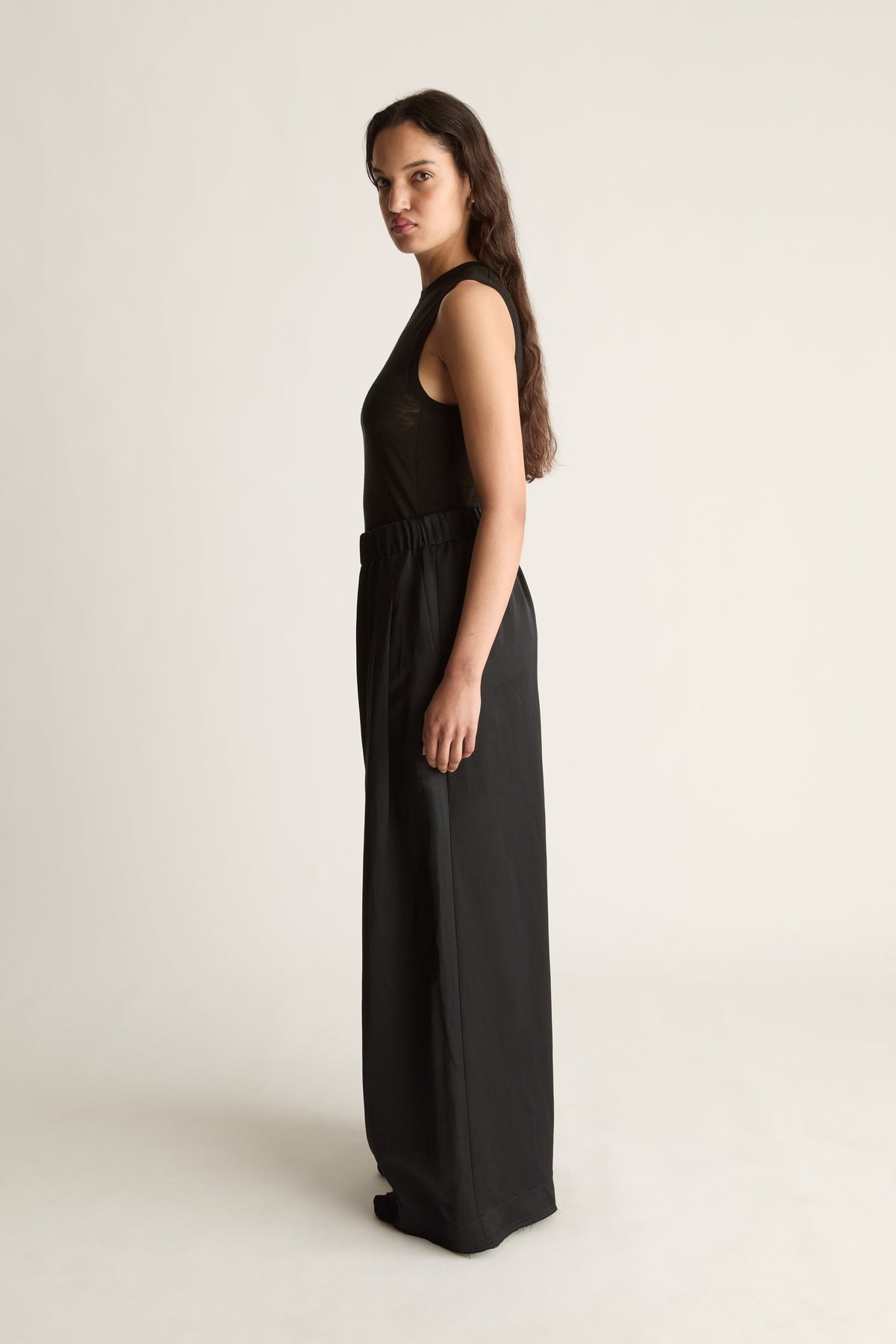 Side view of a woman looking over her shoulder in a black sleeveless top and black wide-leg pants