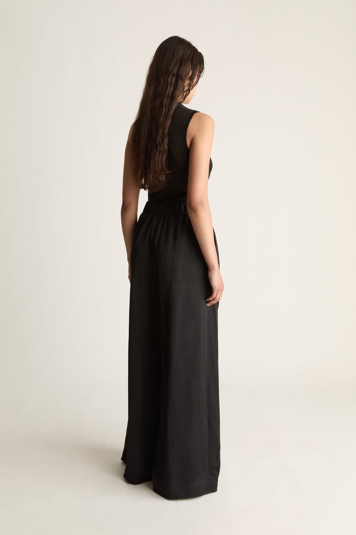 Back view of a woman with long wavy hair in a black sleeveless top and long black wide-leg pants