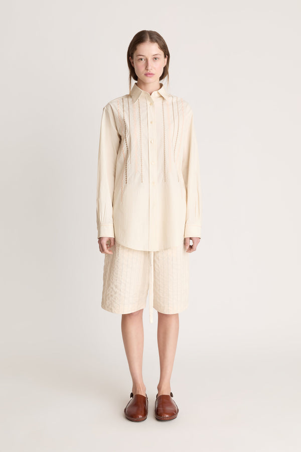 Woman wearing a beige  button up shirt with beige shorts on a white background.