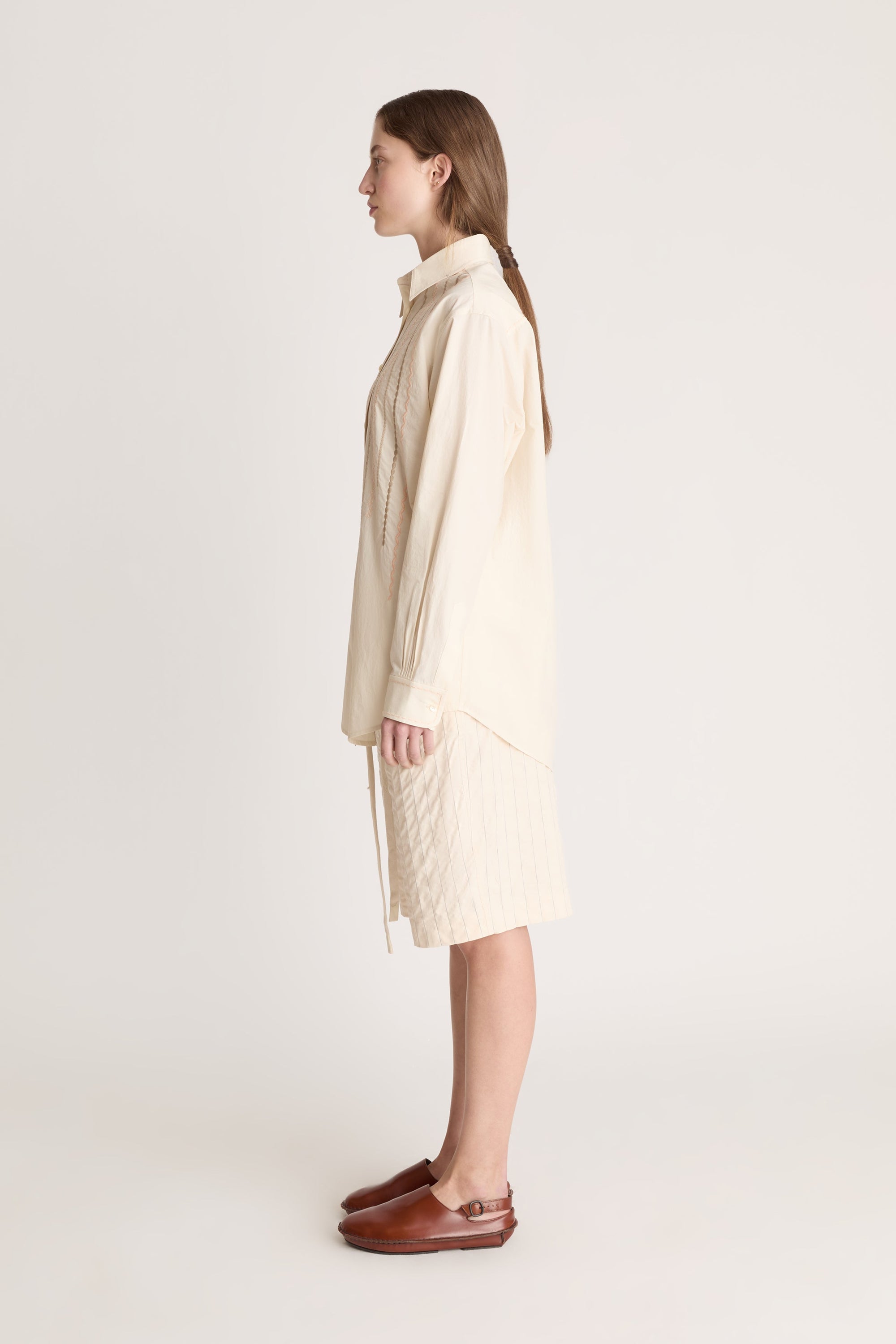 Woman wearing a beige  button up shirt with beige shorts on a white background.