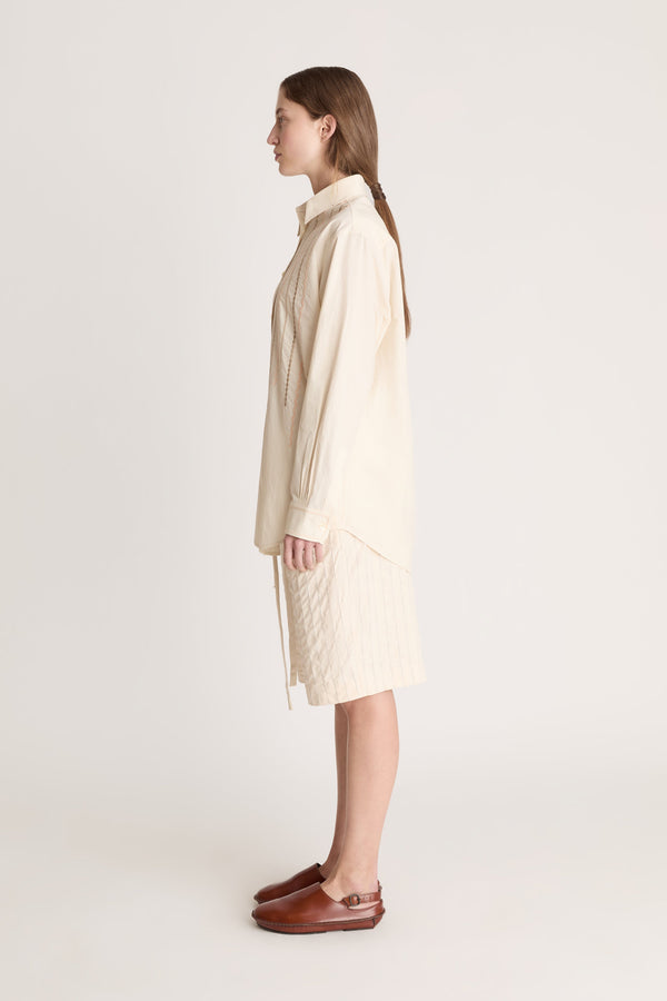 Woman wearing a beige  button up shirt with beige shorts on a white background.