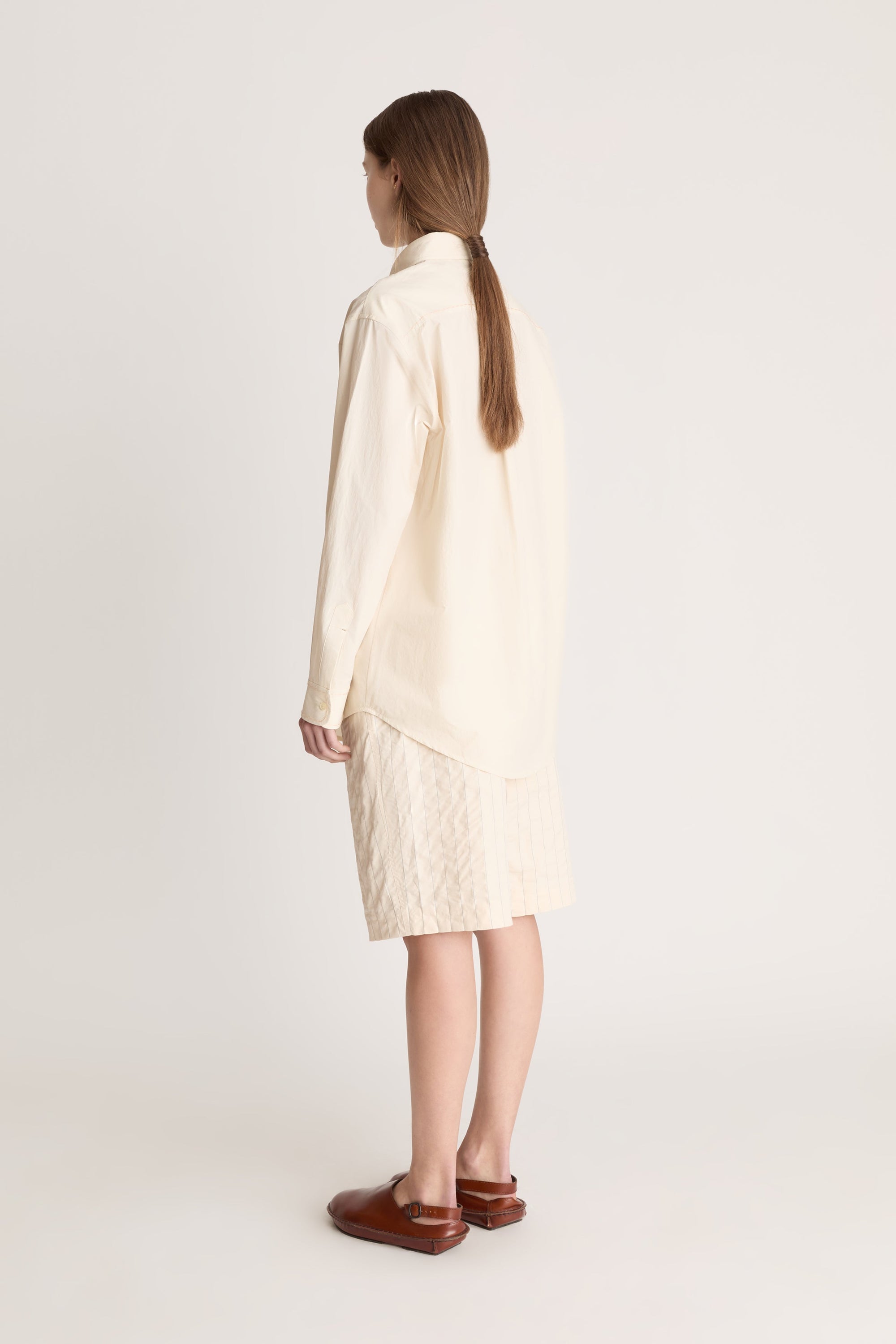 Woman wearing a beige  button up shirt with beige shorts on a white background.