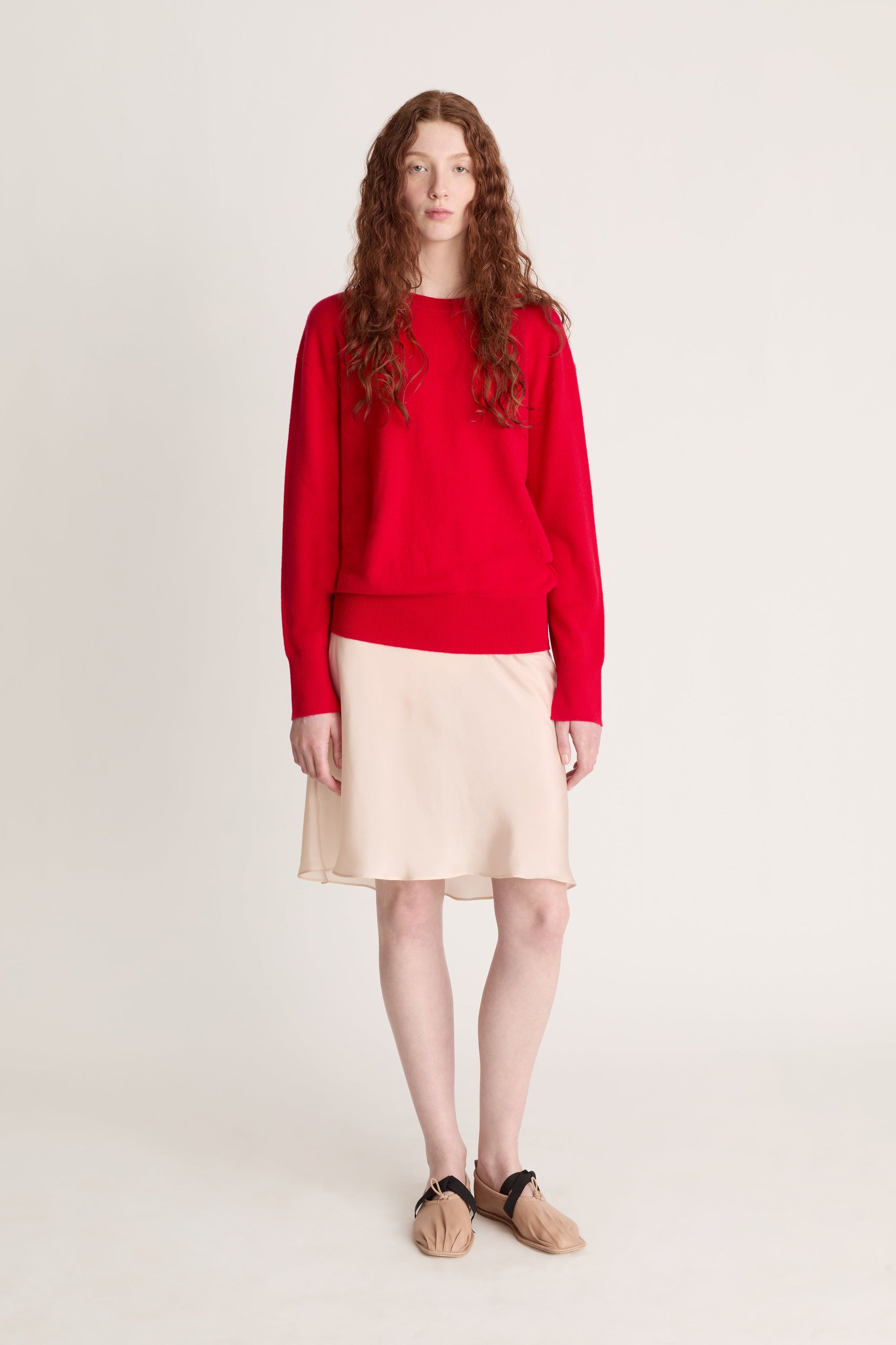 Person wearing a red sweater and beige skirt on a plain background