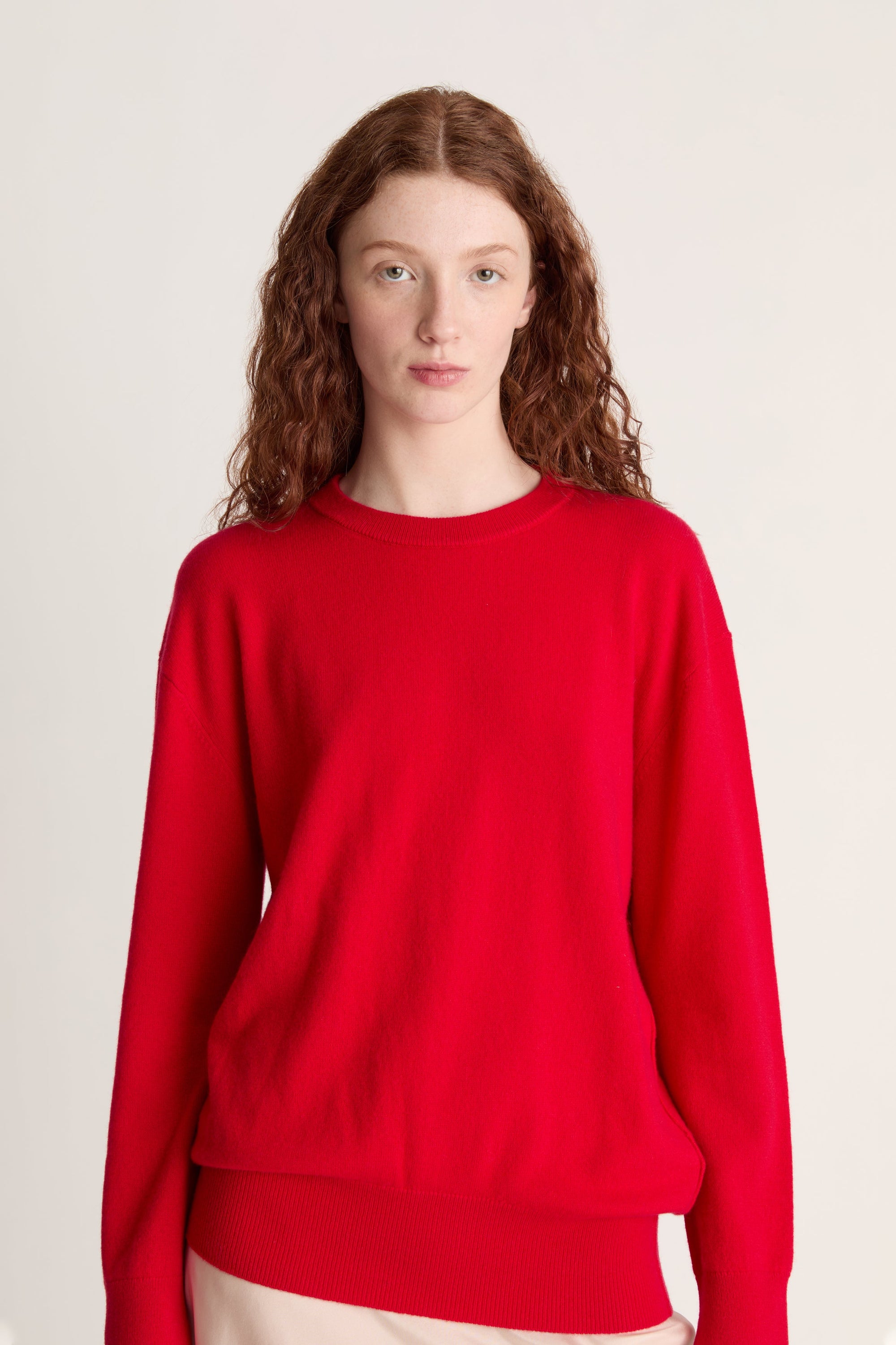 Person wearing a red sweater and beige skirt on a plain background