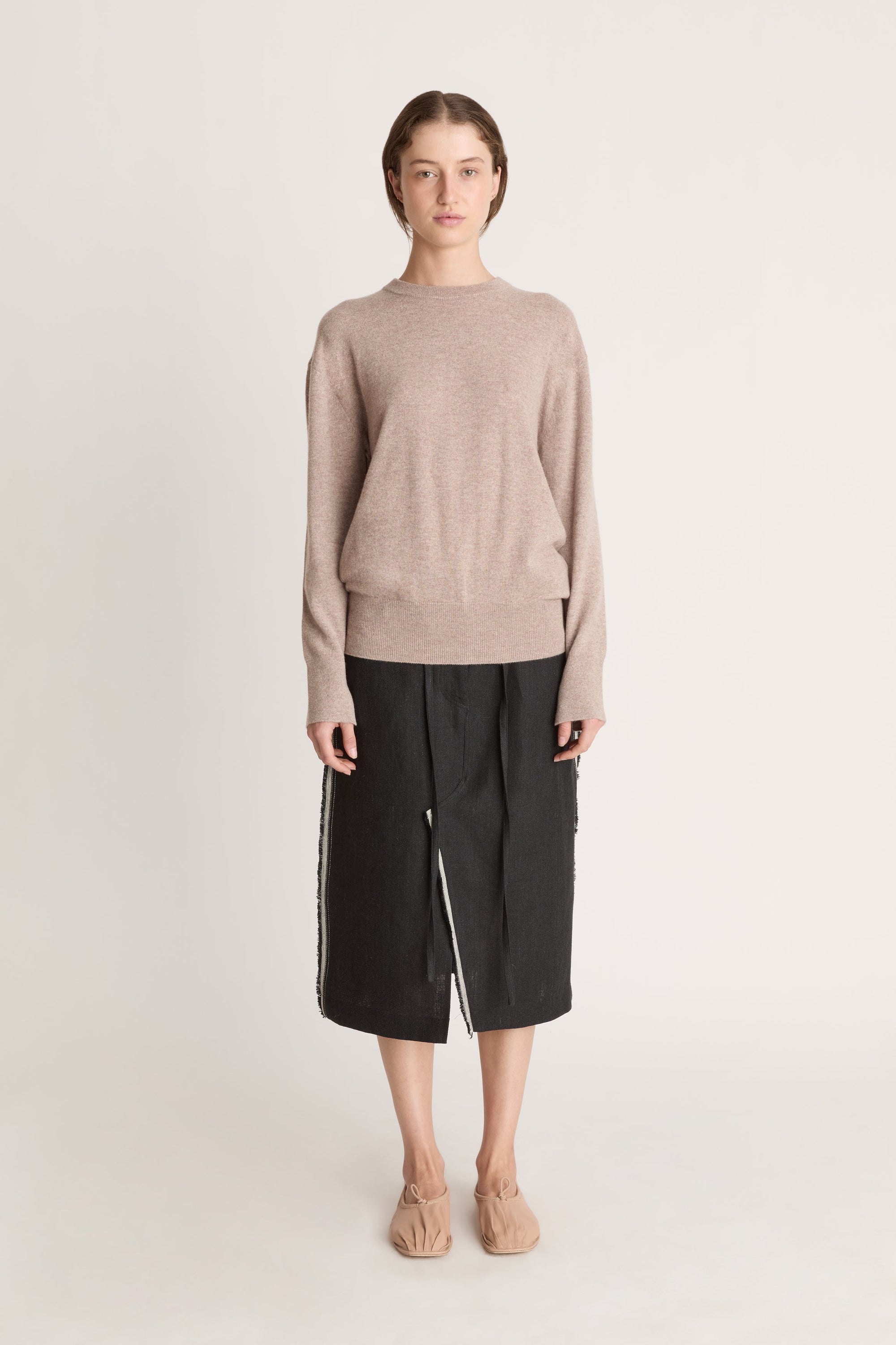 Person wearing a beige sweater and black skirt on a white background