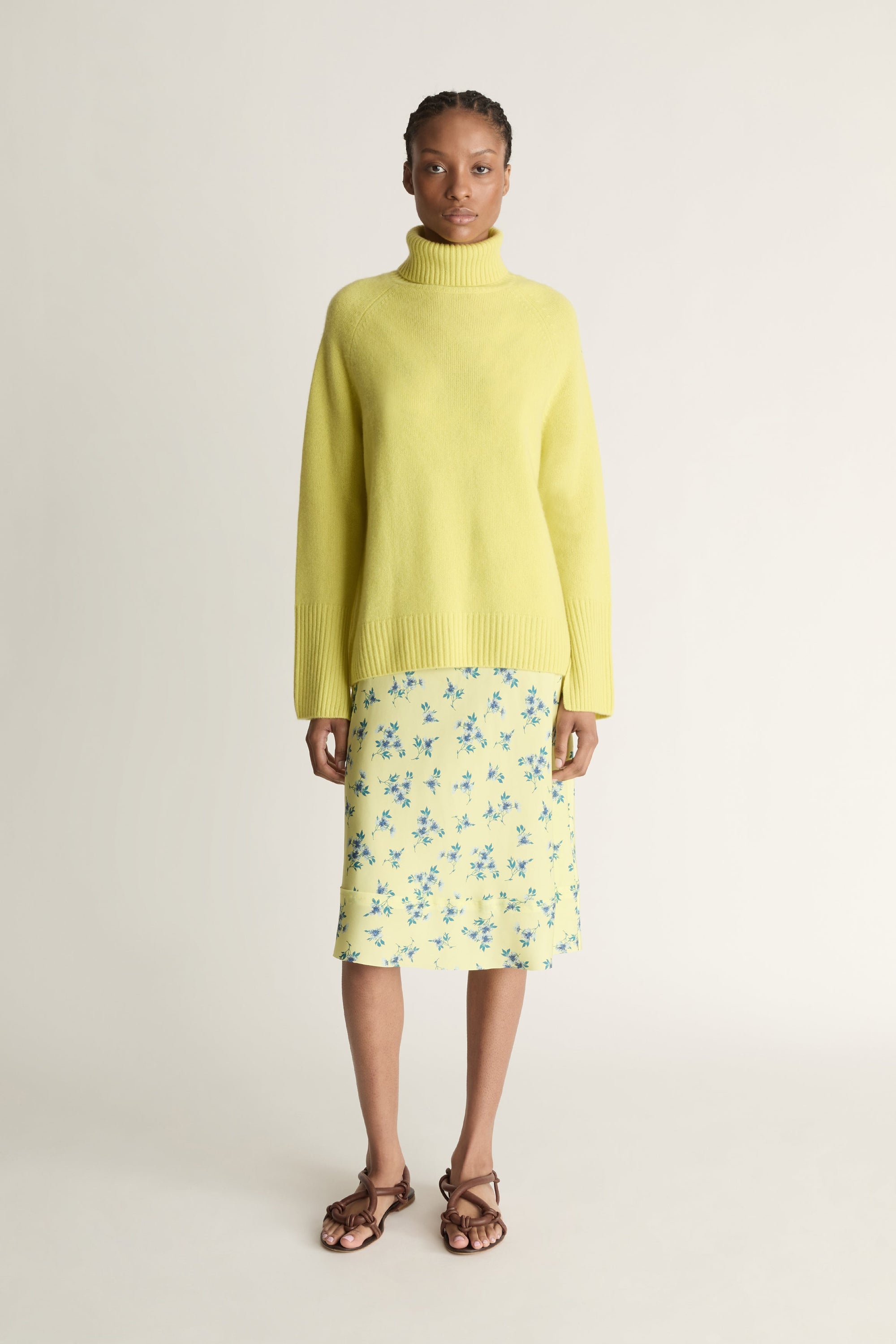 Woman wearing a yellow sweater and floral skirt on a plain background