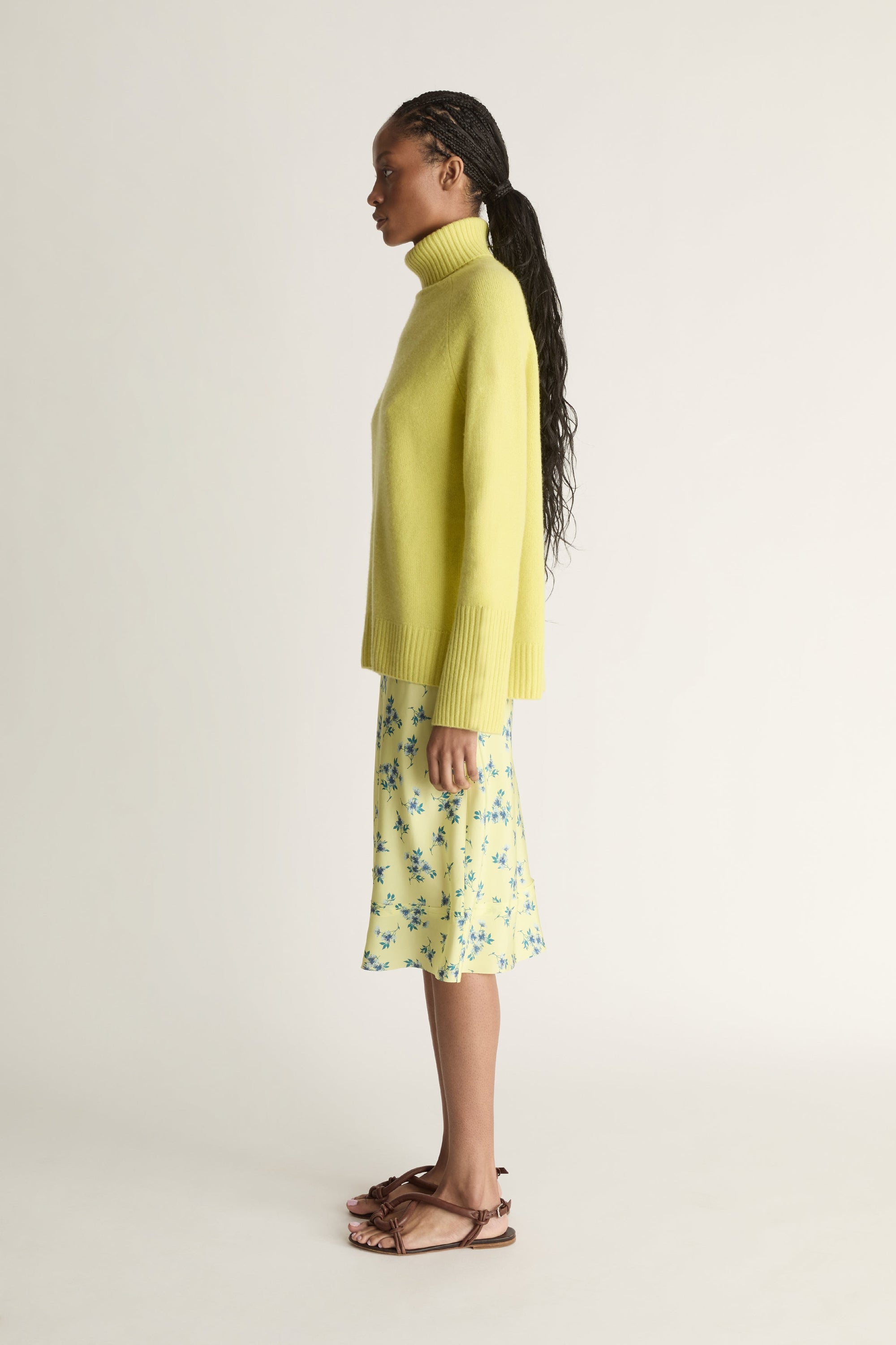 Woman wearing a yellow sweater and floral skirt on a plain background