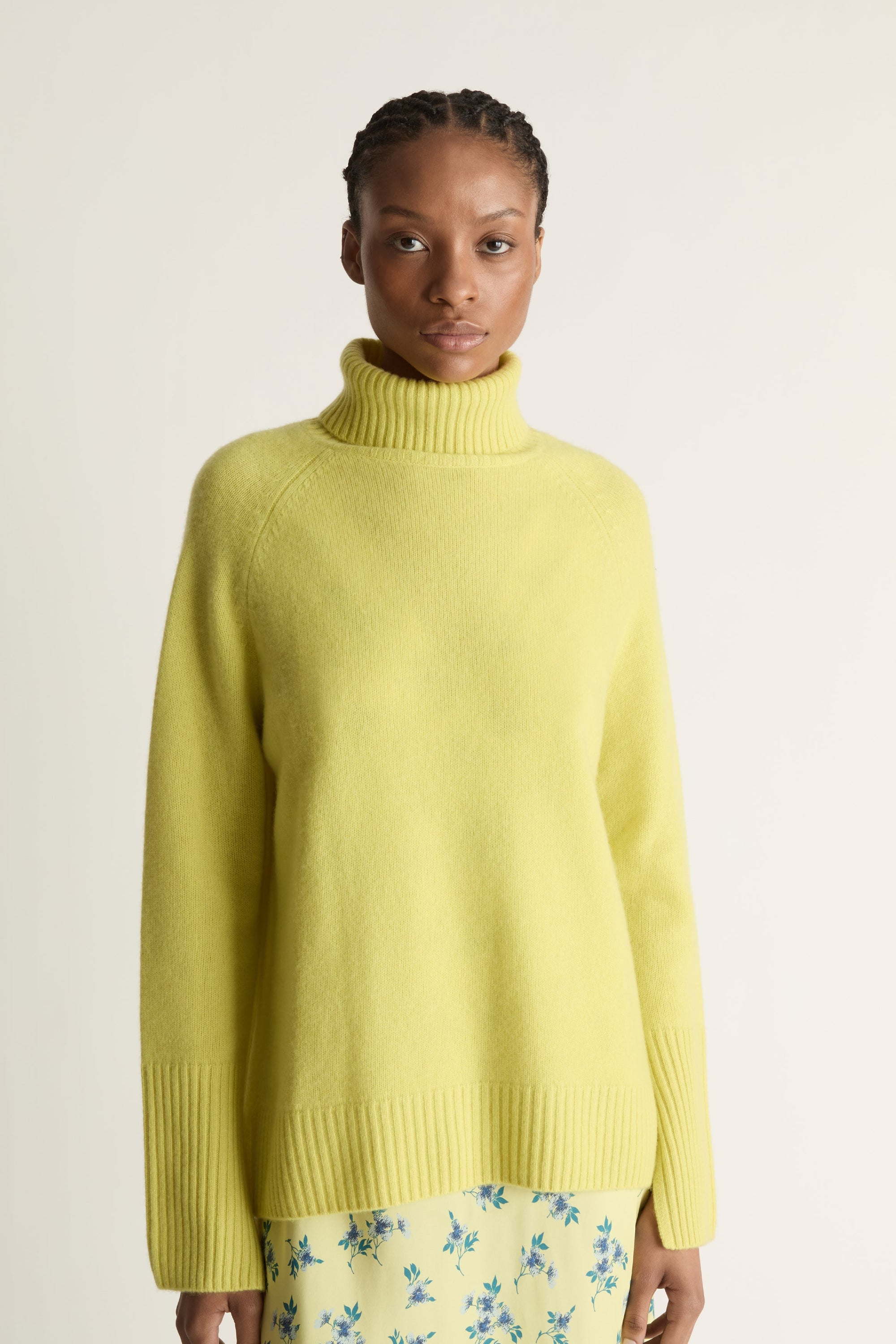 Woman wearing a yellow sweater and floral skirt on a plain background