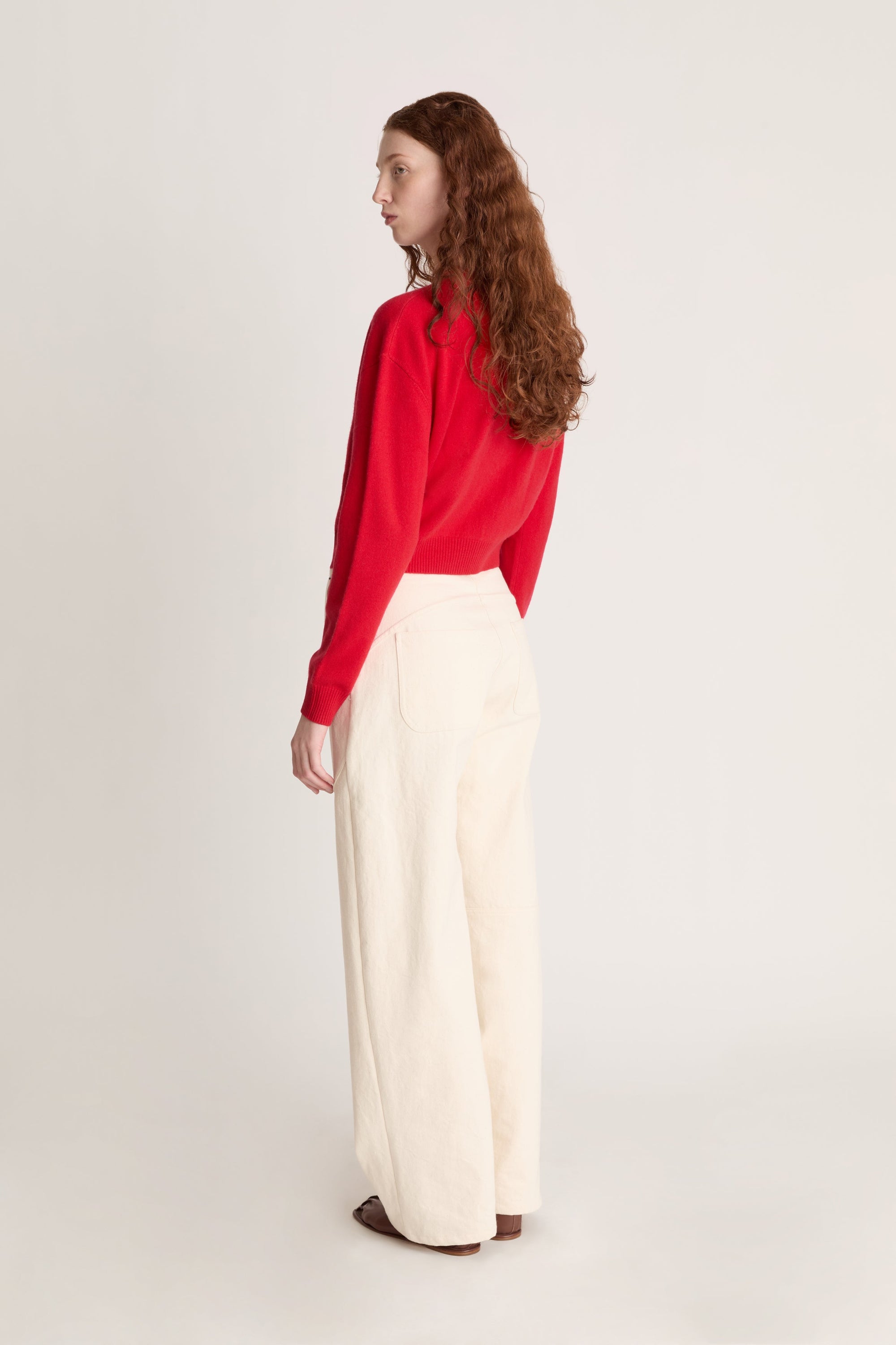 Woman wearing a red cardigan and white pants on a plain background