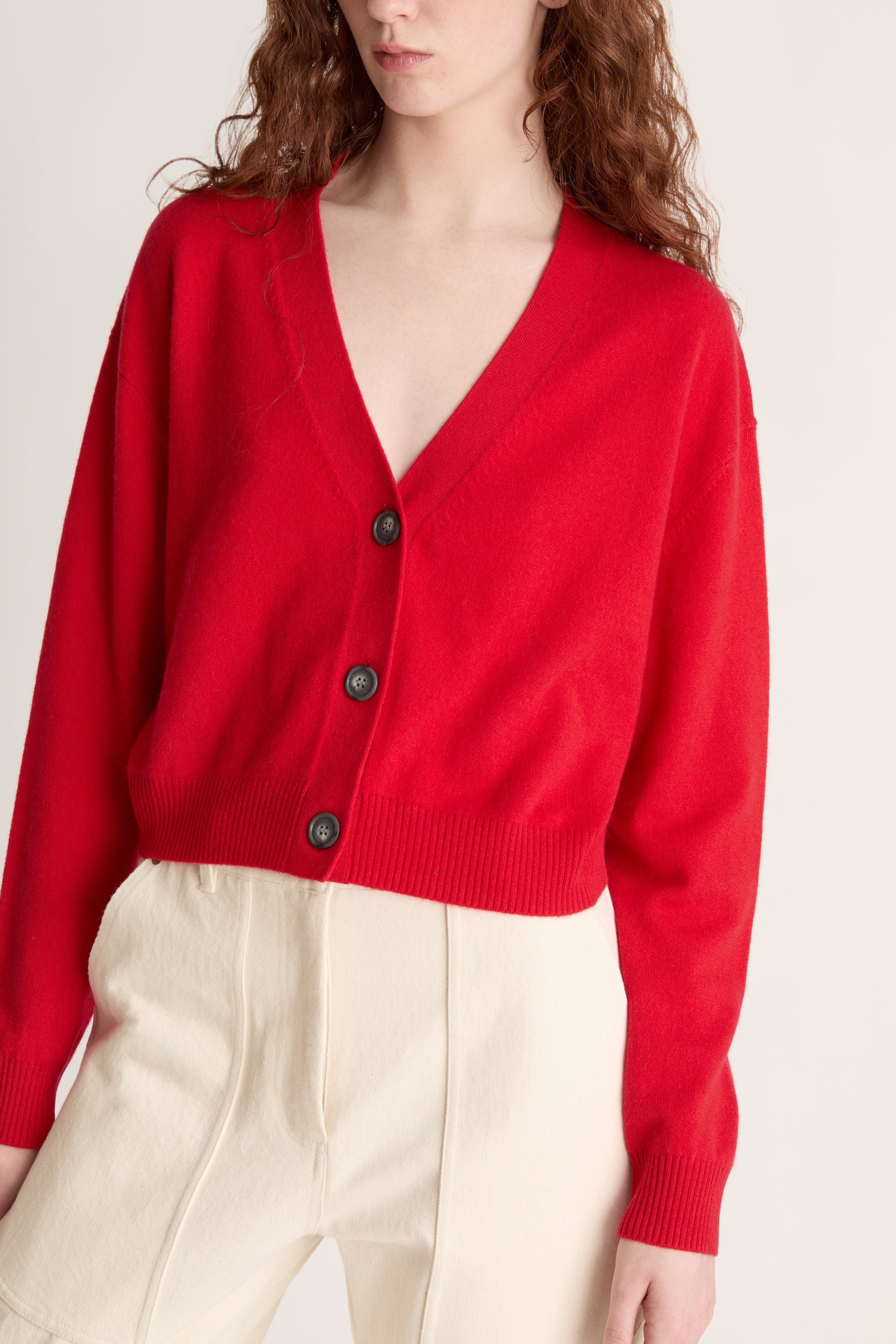 Woman wearing a red cardigan and white pants on a plain background