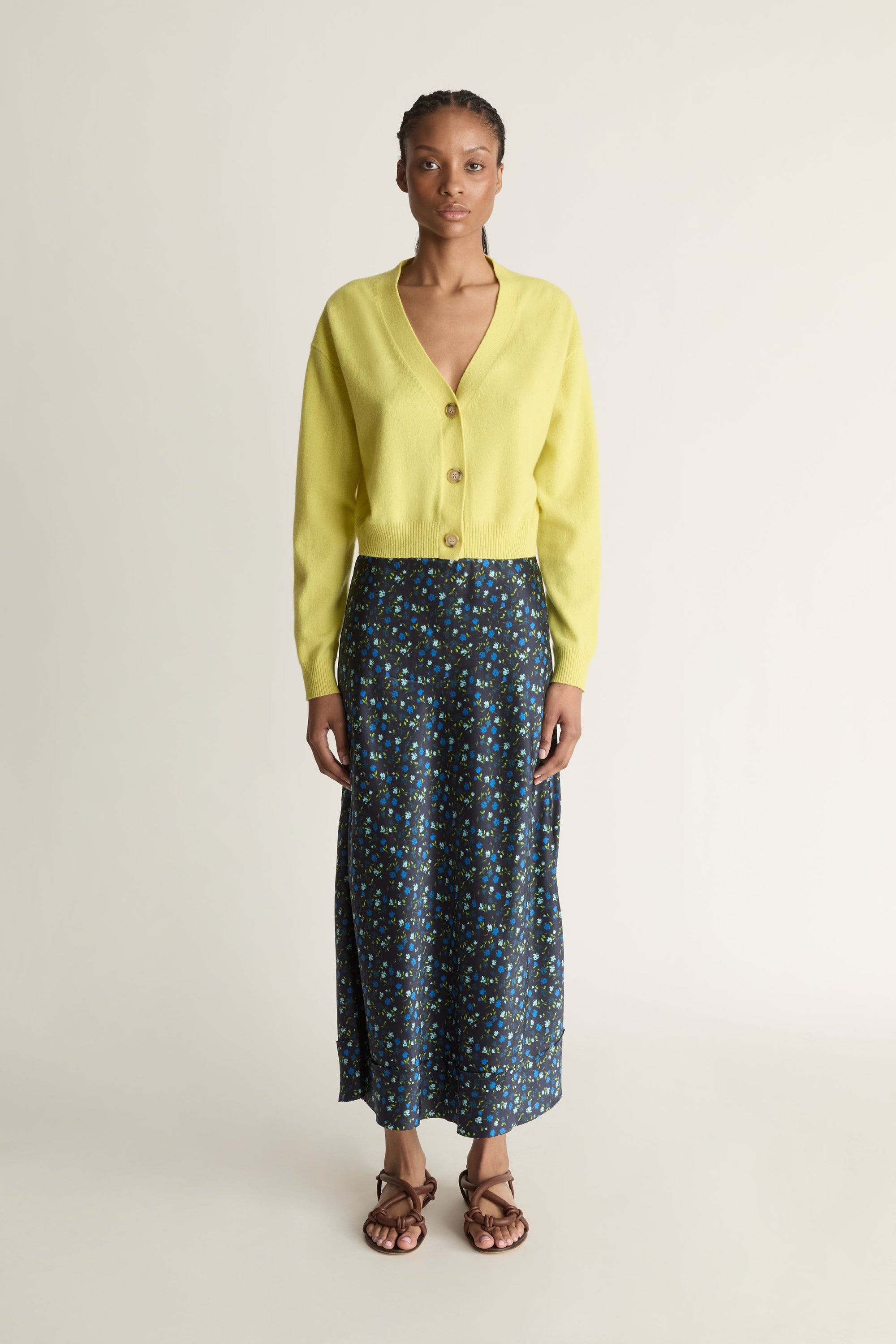 Woman wearing a yellow cardigan and patterned skirt on a white background