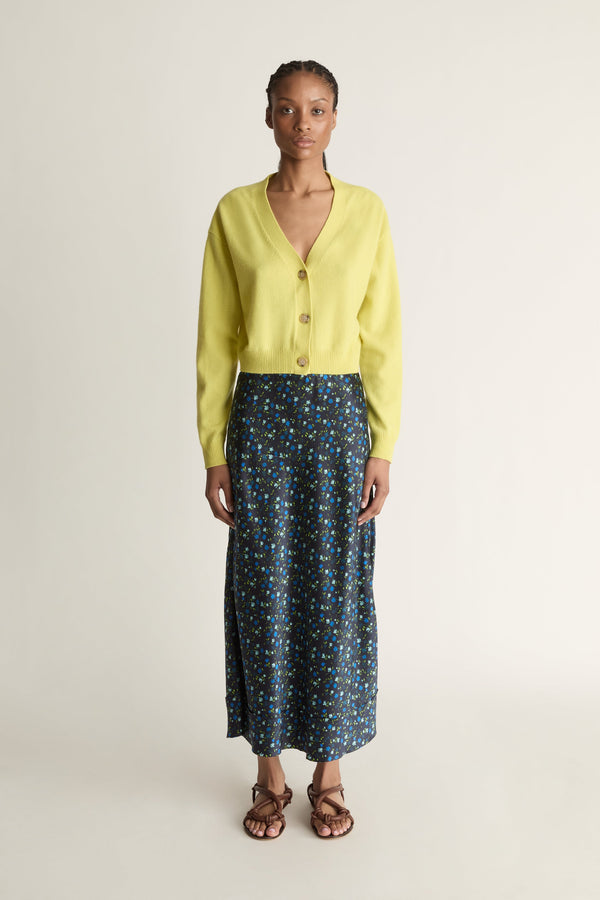Woman wearing a yellow cardigan and patterned skirt on a white background