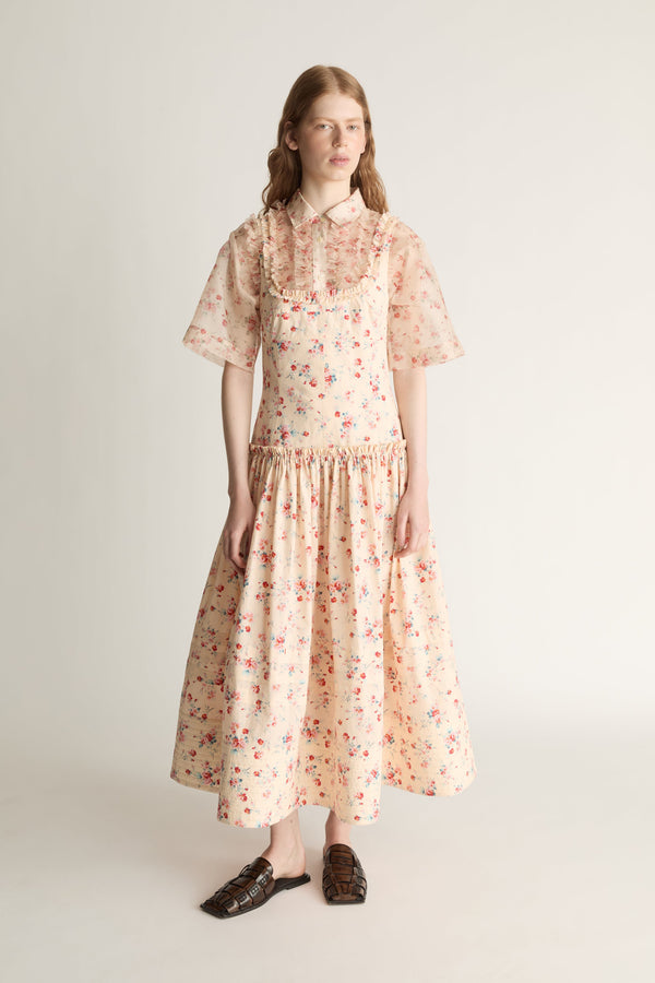 Woman wearing a floral dress over a shirt on a plain background
