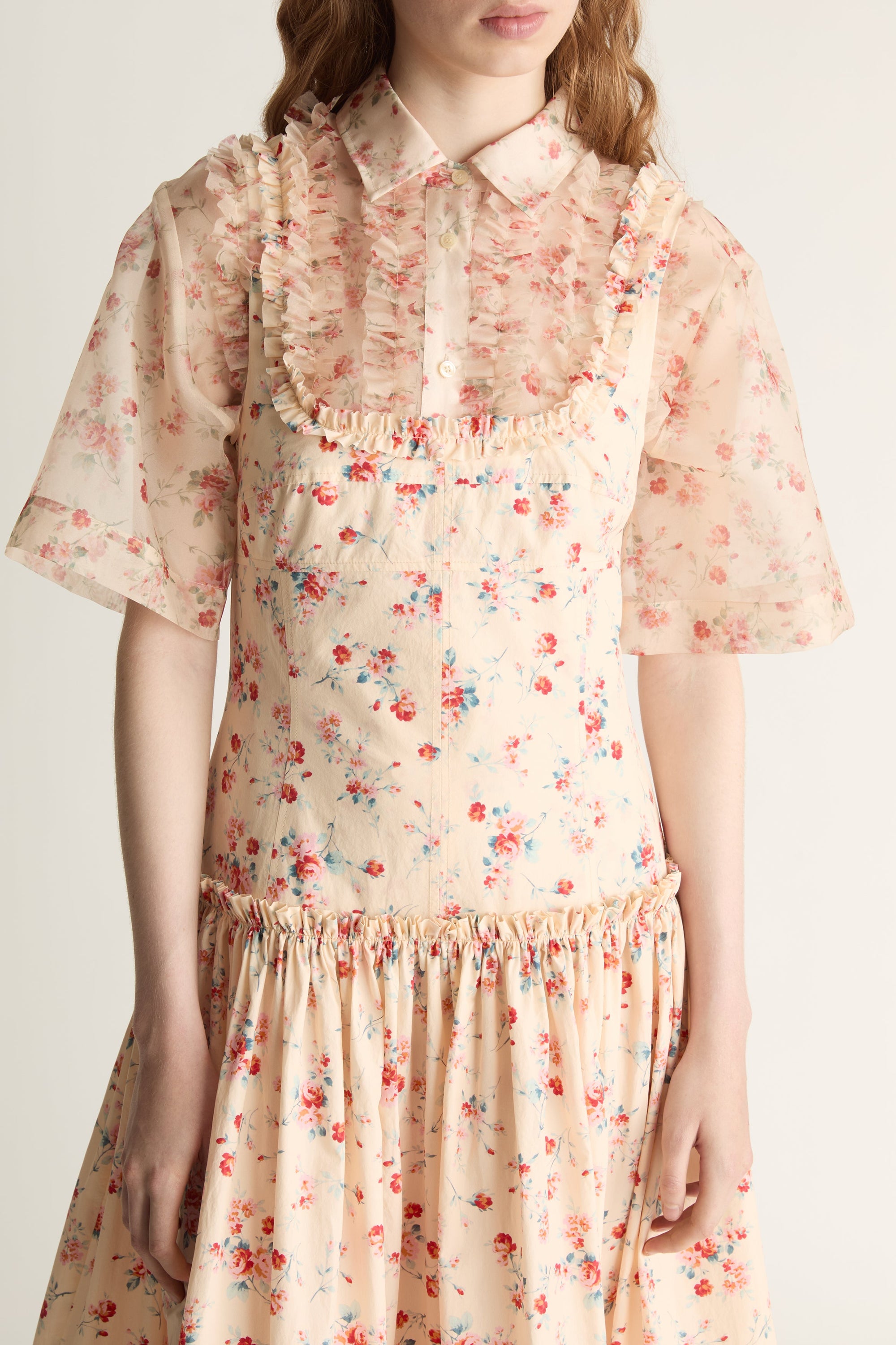 Woman wearing a floral dress over a shirt on a plain background