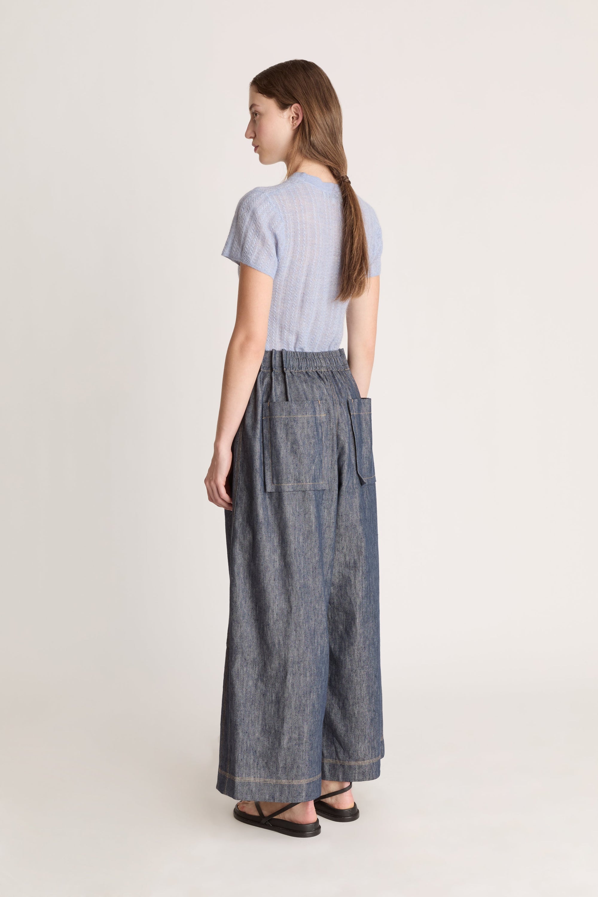 Woman wearing a light blue shirt and dark denim pants on a white background