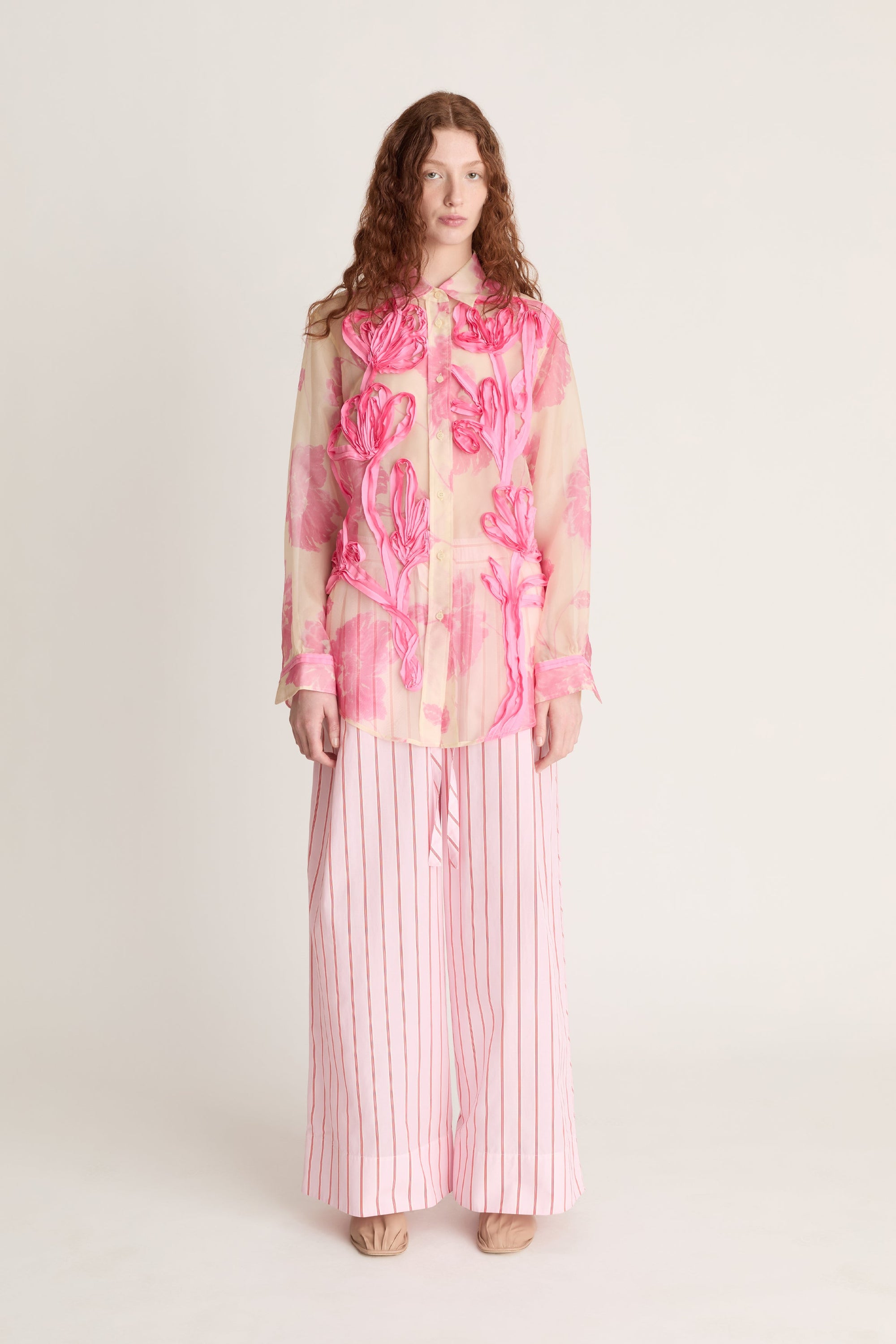 Woman wearing a pink floral blouse and striped pants on a white background