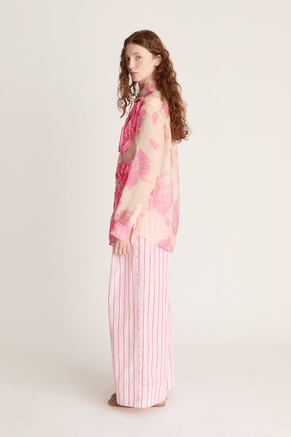 Woman wearing a pink floral top and striped pants on a white background