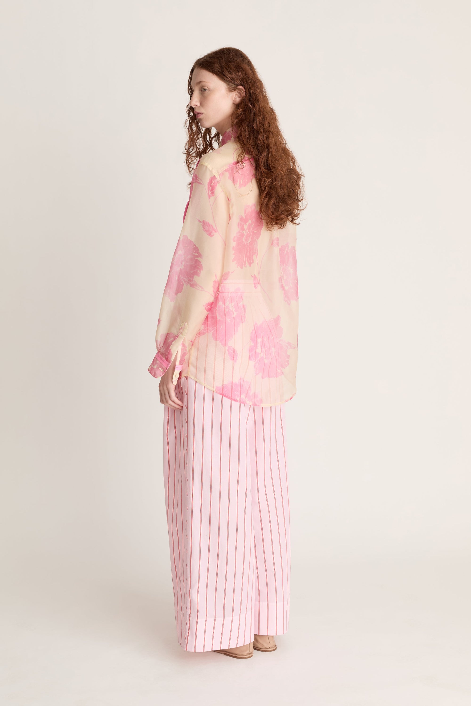 Woman wearing a pink floral blouse and striped pants on a white background