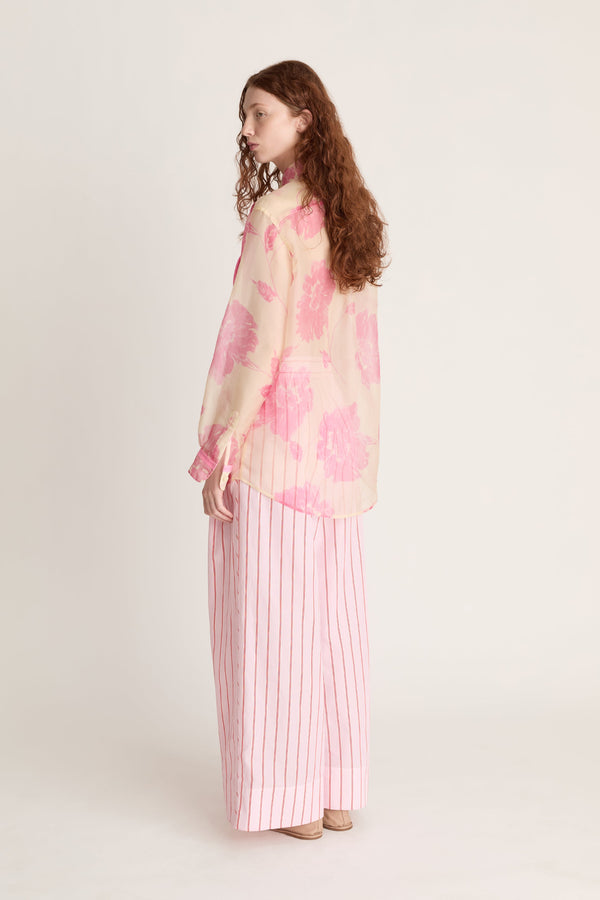 Woman wearing a pink floral blouse and striped pants on a white background