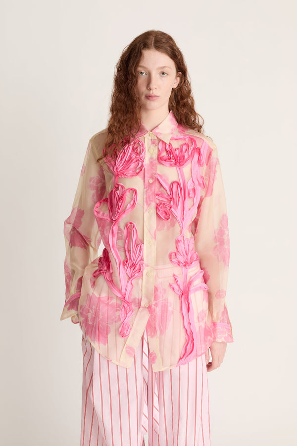 Woman wearing a pink floral sheer blouse with a white background