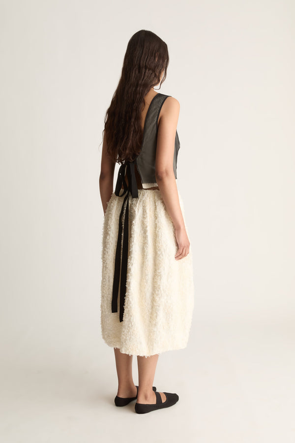 Back view of a cropped sheer black top with an open back tied in a bow with long black ties.