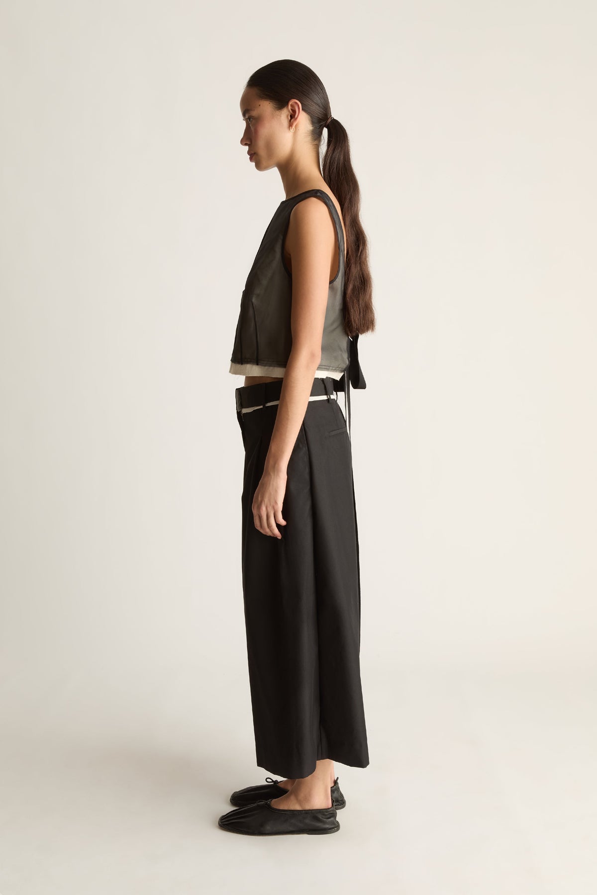 Side view of black wide-leg cropped pants with a pleated front and a hem ending above the ankle.