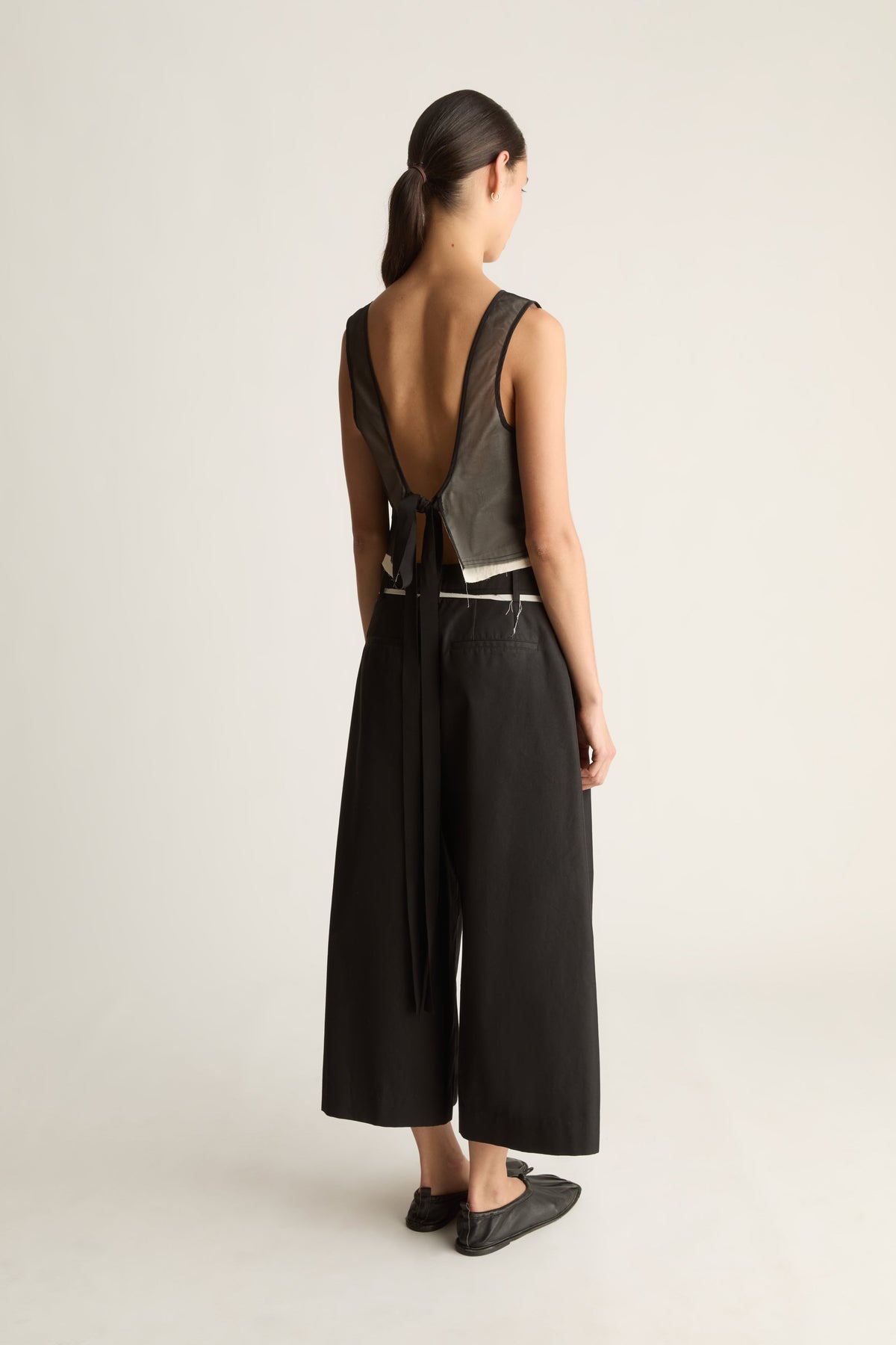 Back view of black wide-leg cropped pants with a cream-edged waistband, worn with an open-back top.