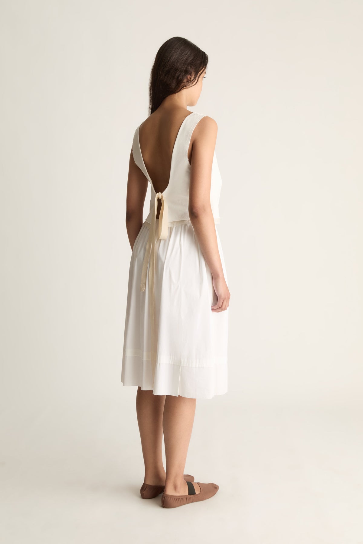 Back view of a cropped cream top with a deep open back tied at the waist.