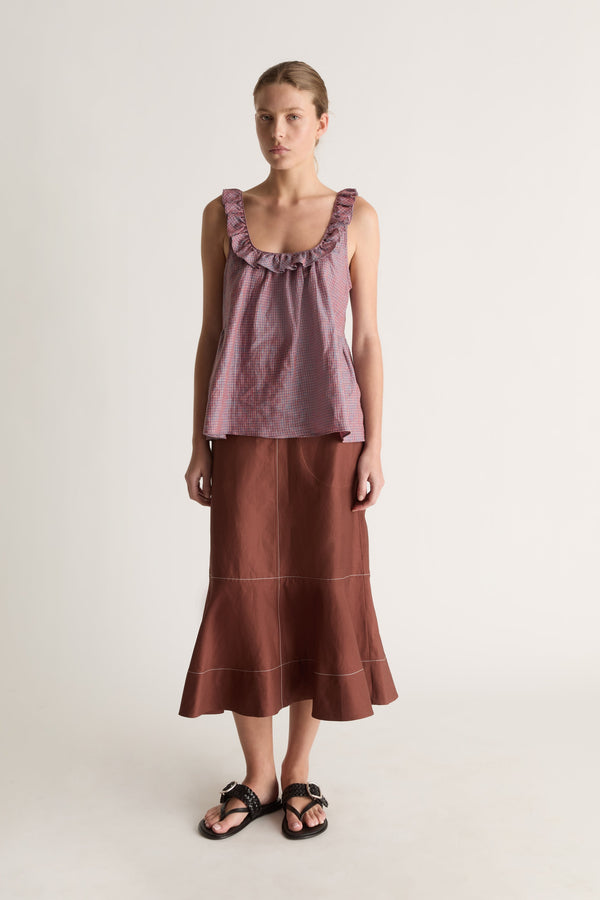 Front view of a woman with hair pulled back in a plum check cami top, brown topstitched midi skirt and black sandals