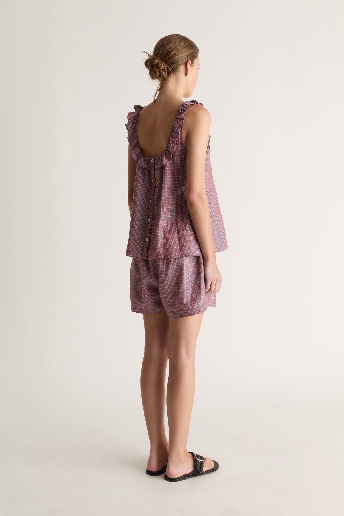 Back view of a woman with a bun in plum check shorts and a ruffle-strap top with scoop back and button closure