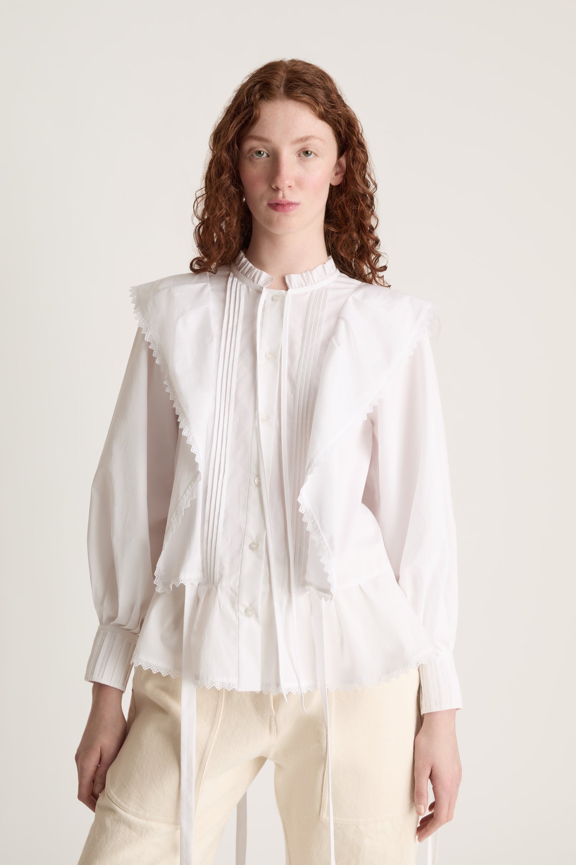 Woman wearing a white blouse and beige pants on a plain background