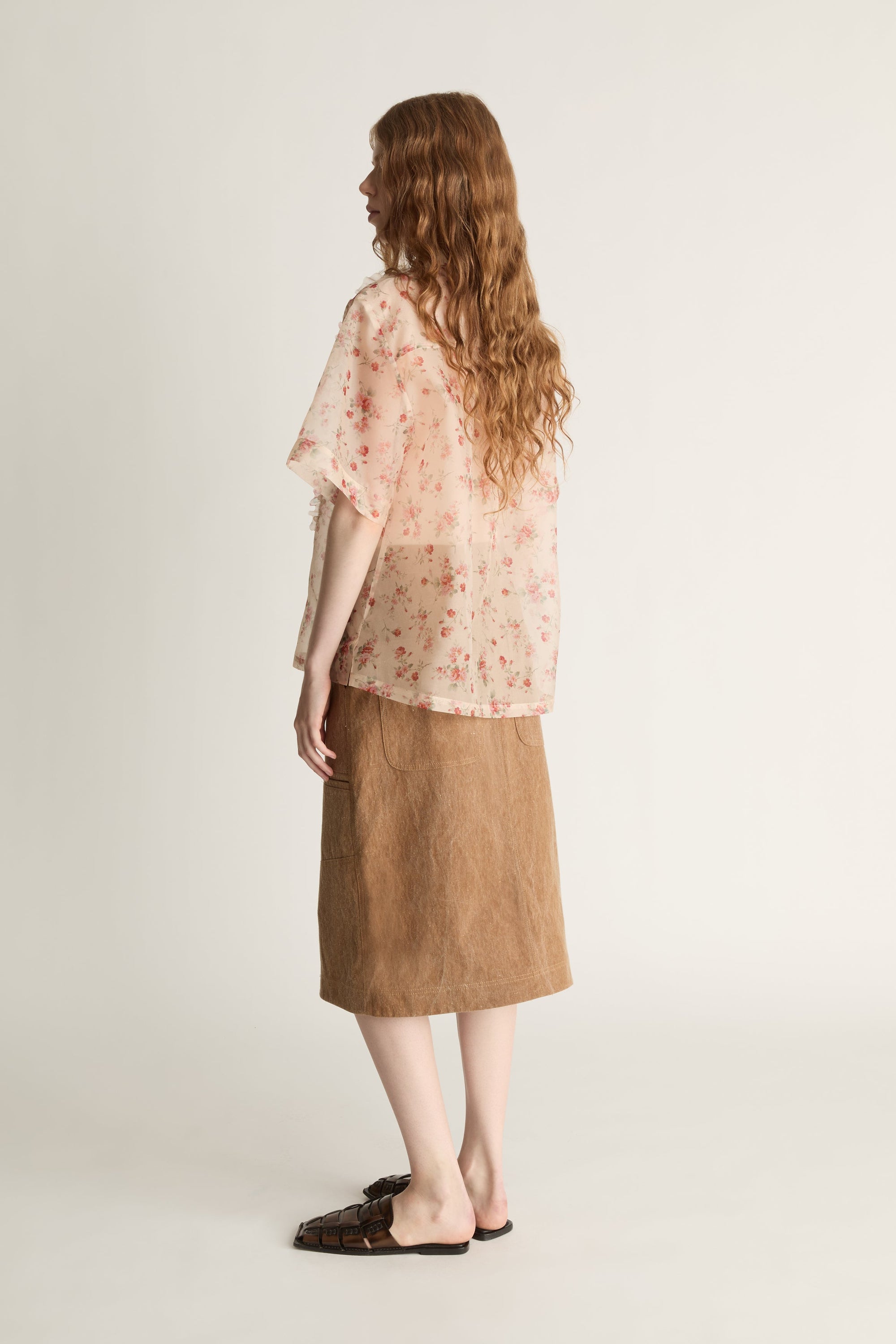Person wearing a floral blouse and brown skirt on a white background