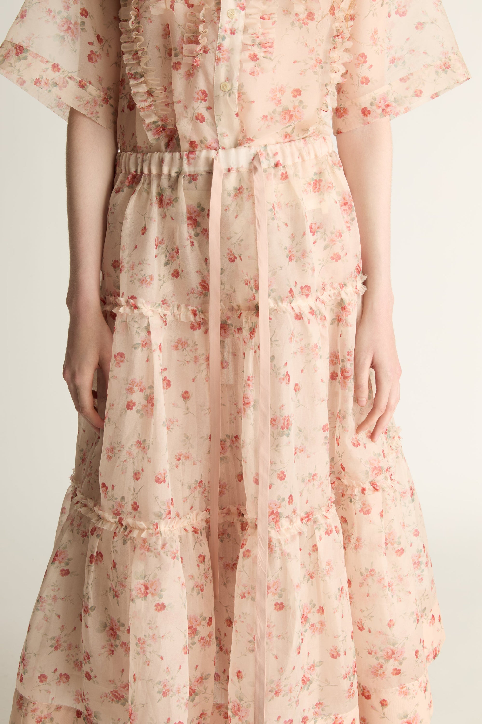 A woman wearing a floral shirt and skirt on a plain background