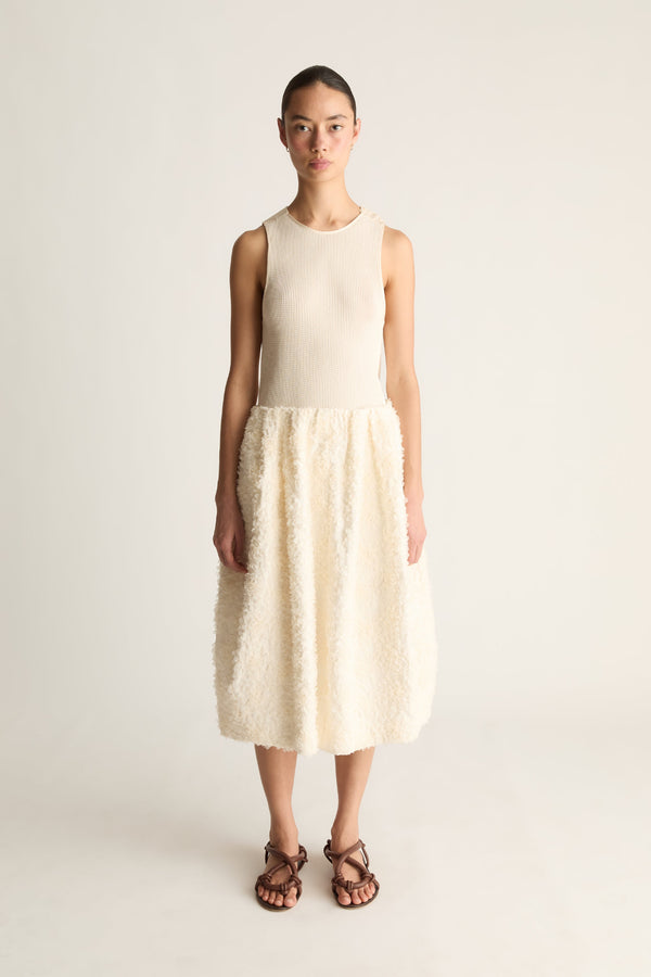 Front view of a woman wearing a cream sleeveless top and cream textured cocoon midi skirt against a white studio background