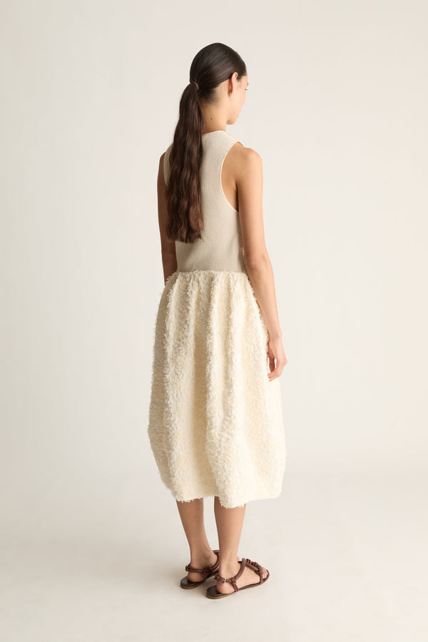 Back view of a woman with a long ponytail in a cream tank top and textured balloon midi skirt