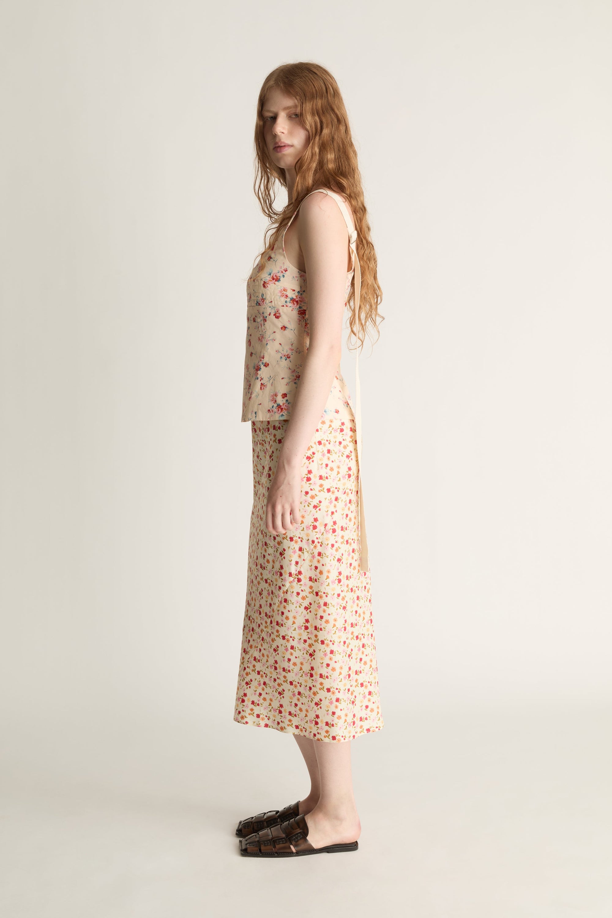 A woman wearing a floral blouse and skirt  on a plain background