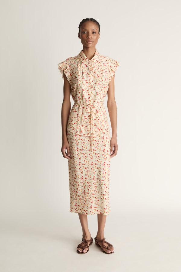 A woman wearing a floral shirt and skirt on a plain background