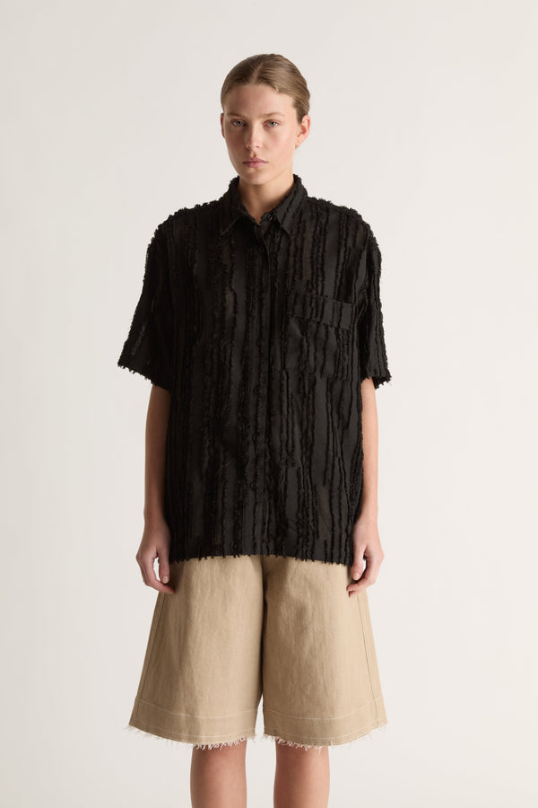 Close-up of a black fringed-stripe short-sleeve shirt with chest pocket and collar