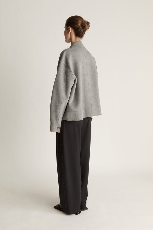 Person wearing a gray jacket and black pants on a white background