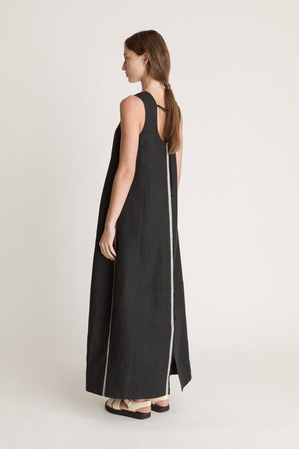 Woman wearing a black sleeveless dress with astripe down the front on a white background
