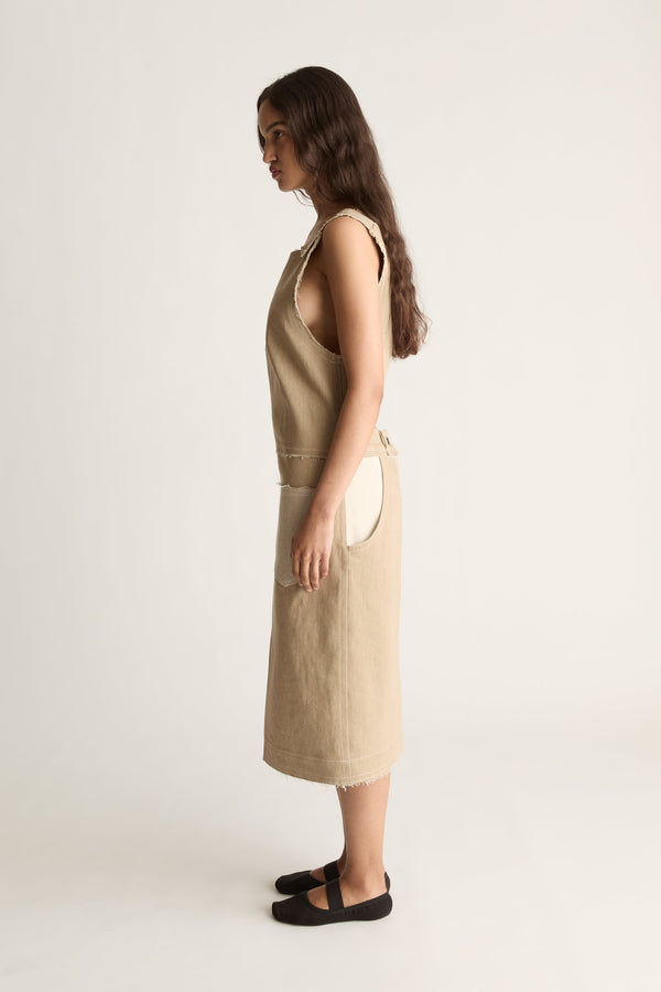 Side profile of a woman with long dark hair in a beige sleeveless midi dress and black ballet flats