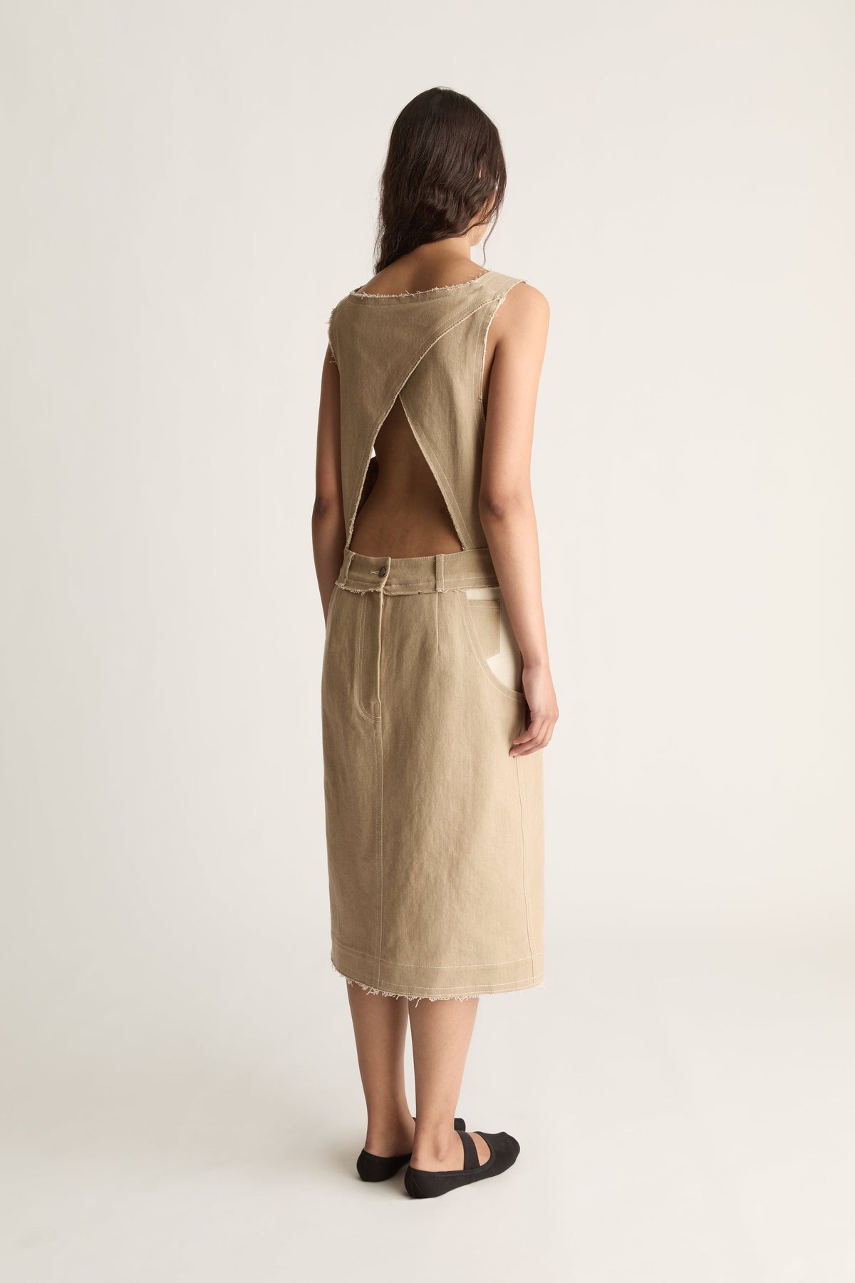 Back view of a woman in a beige midi dress with criss-cross open back and frayed hem