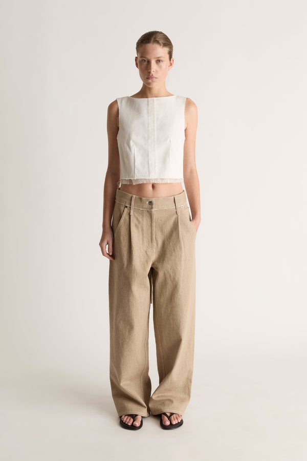 Front view of a woman wearing a white sleeveless cropped top and beige pleated wide-leg jeans against a white studio background