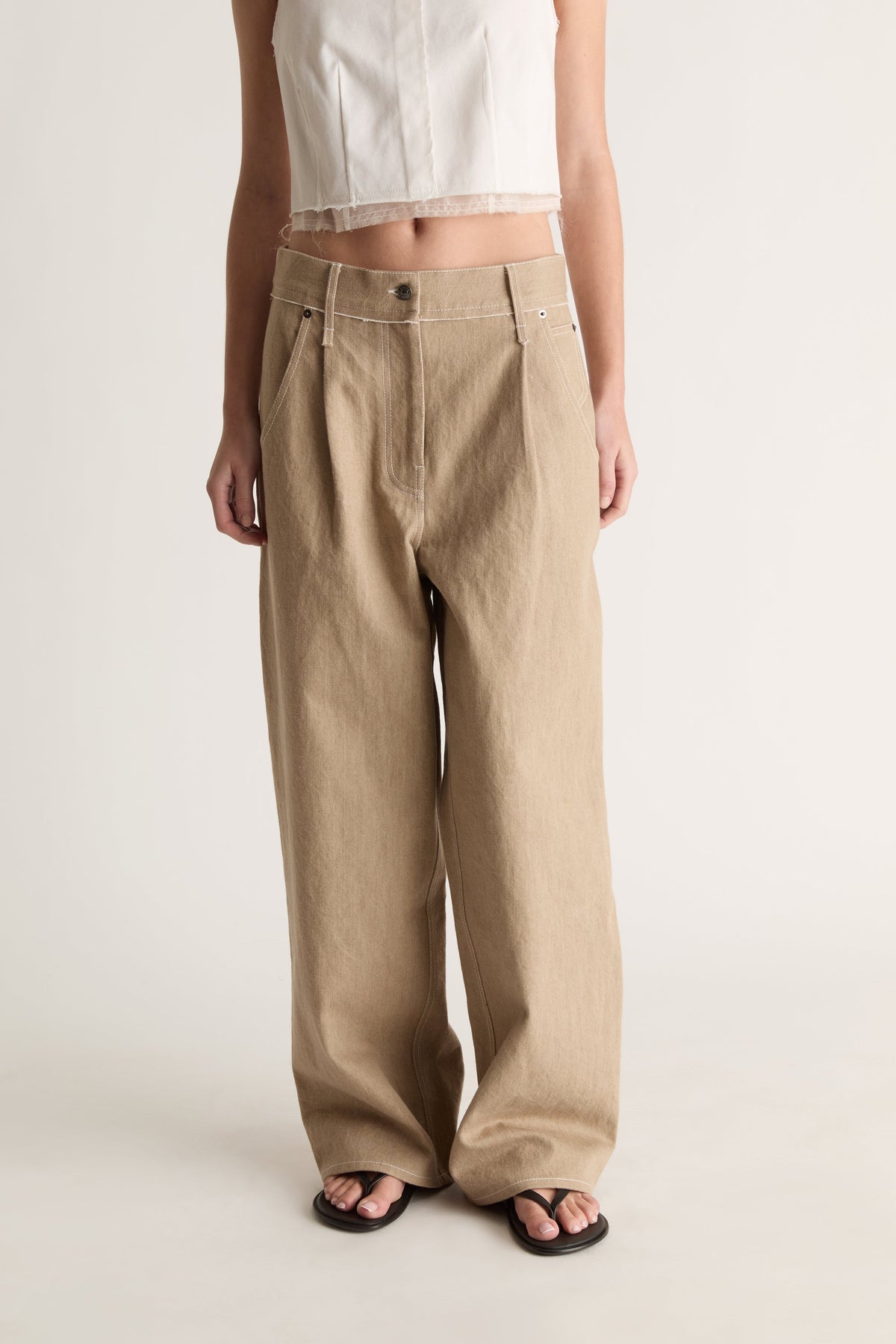 Close-up of beige high-waisted wide-leg jeans with front pleats and button closure, worn with a white crop top