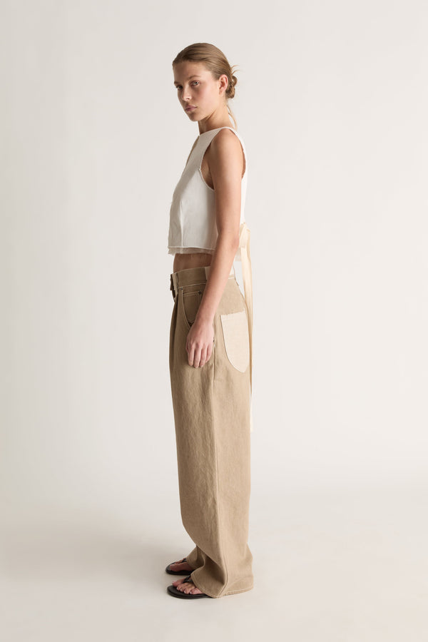 Side view of a woman in a white sleeveless top and beige wide-leg jeans with cream pocket and black sandals