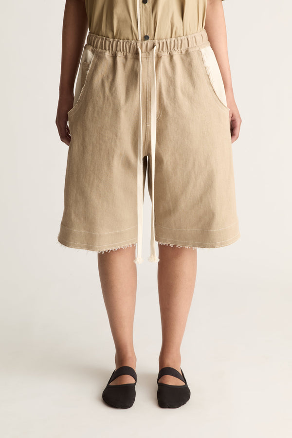 Close-up of beige elastic-waist bermuda shorts with long cream drawstring, cream pockets and frayed hem
