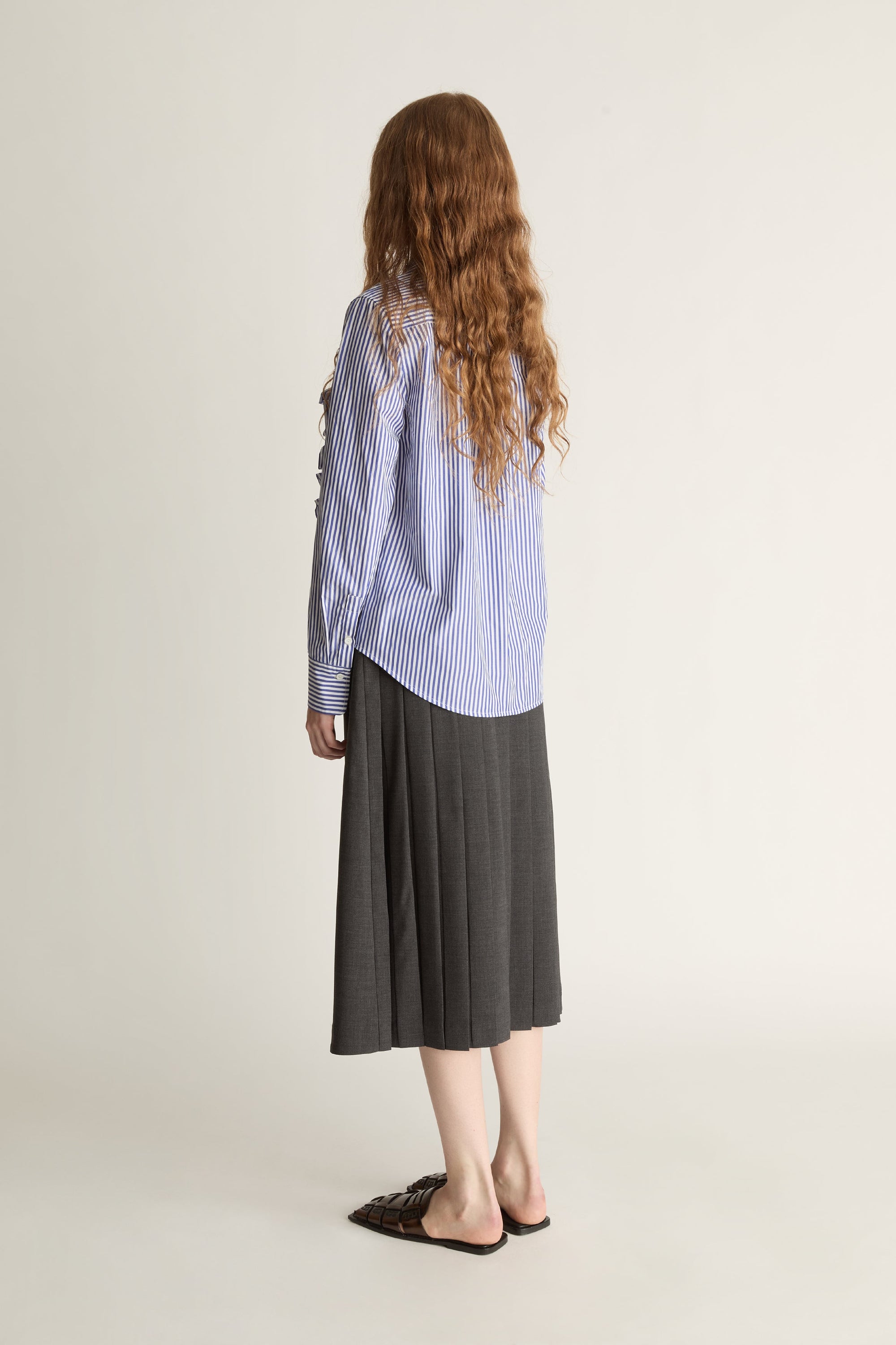 Woman wearing a blue striped shirt with ruffles and a gray skirt on a white background