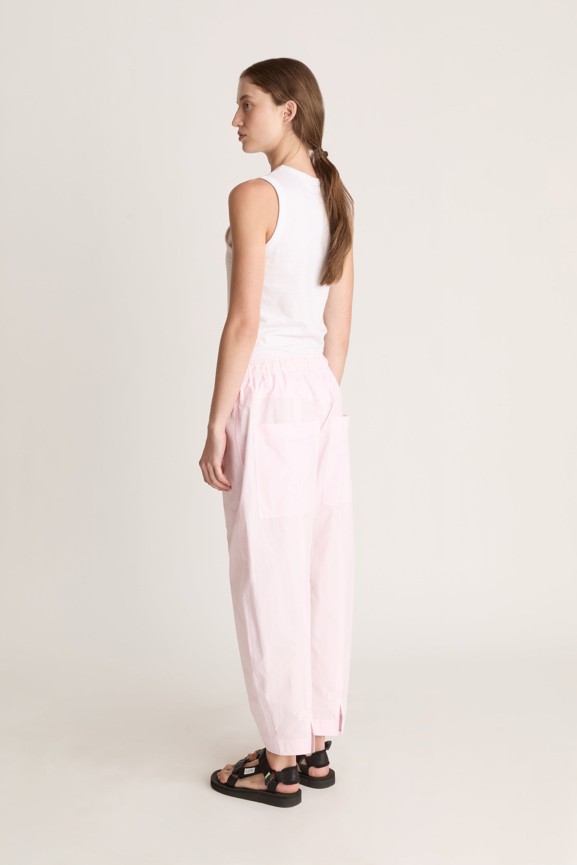 Woman wearing a white sleeveless top and light pink pants on a white background