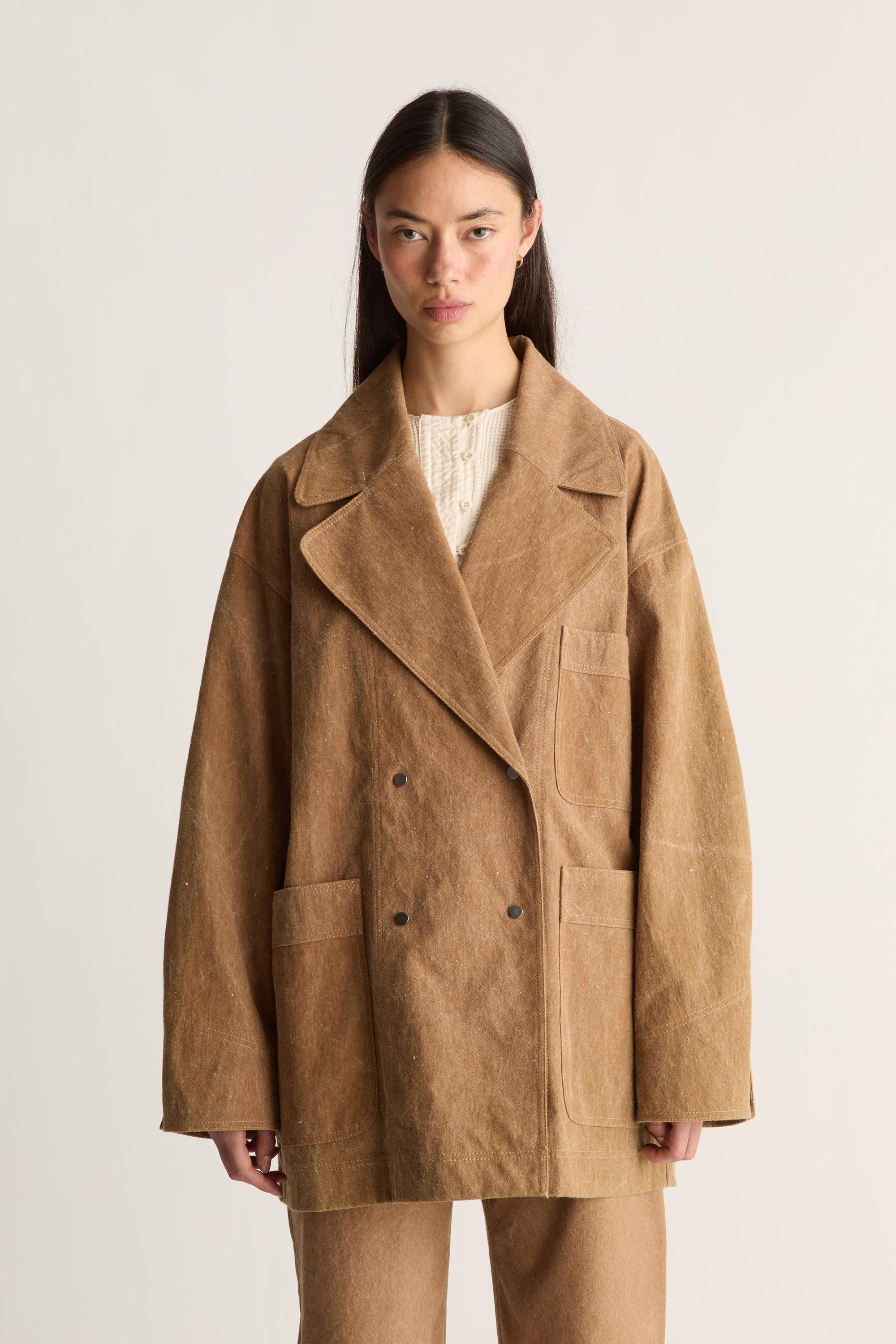Woman wearing a brown coat and pants on a white background, facing the front, zoomed in.